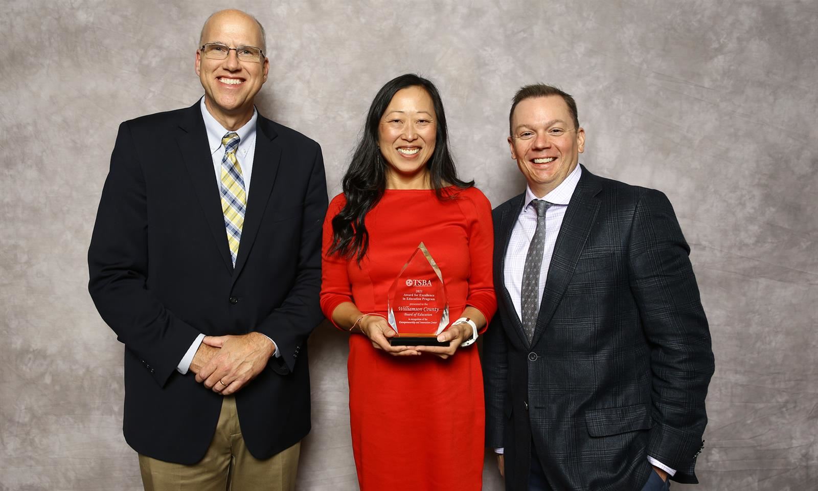 Three adults smile while holding a glass trophy